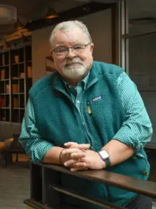 a man with glasses and a green vest leaning on a railing